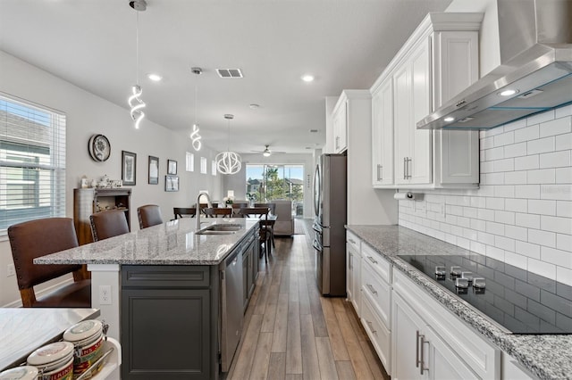 kitchen with appliances with stainless steel finishes, sink, wall chimney range hood, a center island with sink, and white cabinetry