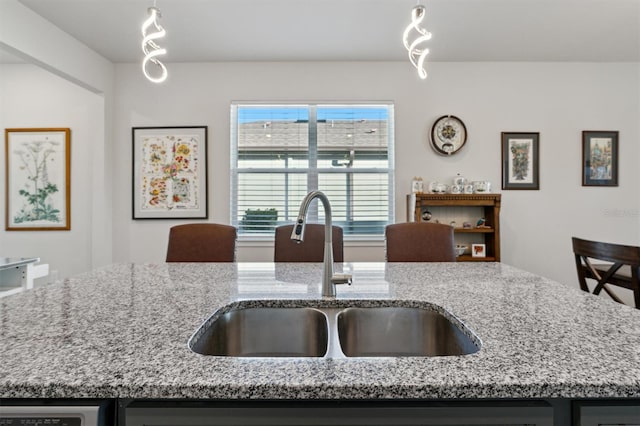 kitchen with light stone countertops, an island with sink, hanging light fixtures, and sink