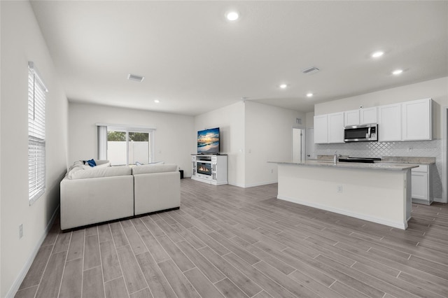 kitchen featuring white cabinets, light wood-type flooring, backsplash, and an island with sink