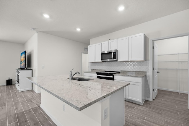 kitchen featuring an island with sink, light stone countertops, sink, white cabinetry, and black / electric stove