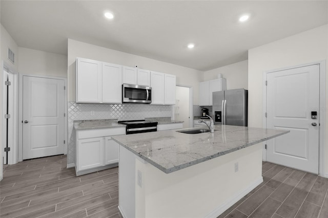 kitchen with light stone counters, stainless steel appliances, an island with sink, white cabinets, and sink