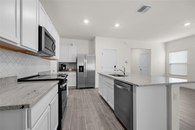 kitchen featuring stainless steel appliances, sink, white cabinetry, light stone counters, and a center island with sink