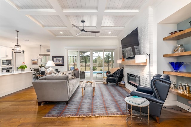 living room featuring dark wood-type flooring, coffered ceiling, a brick fireplace, beamed ceiling, and ceiling fan