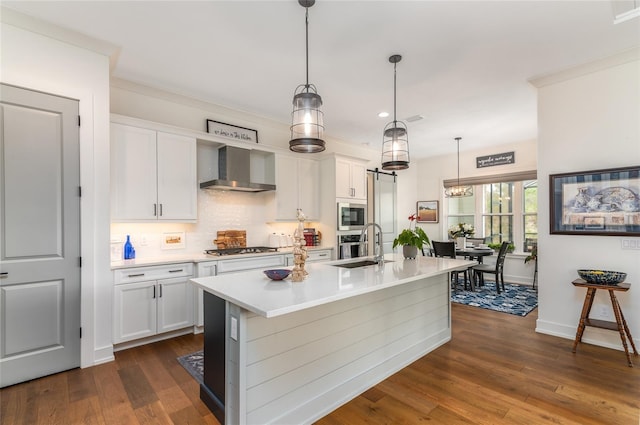 kitchen with pendant lighting, wall chimney range hood, white cabinetry, a kitchen island with sink, and built in microwave