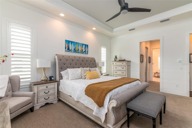 bedroom featuring light carpet, ensuite bath, a raised ceiling, and ceiling fan