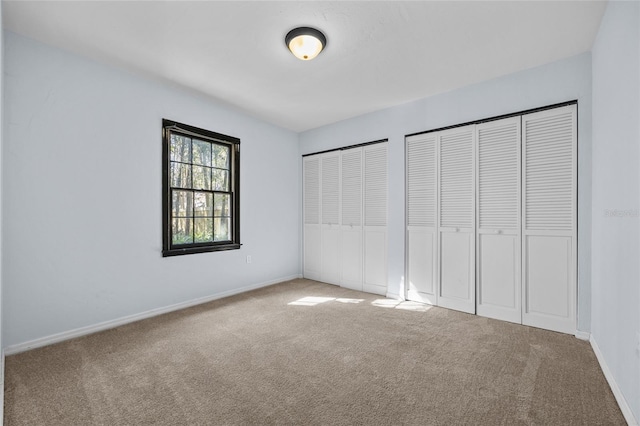 unfurnished bedroom with carpet floors, two closets, and baseboards