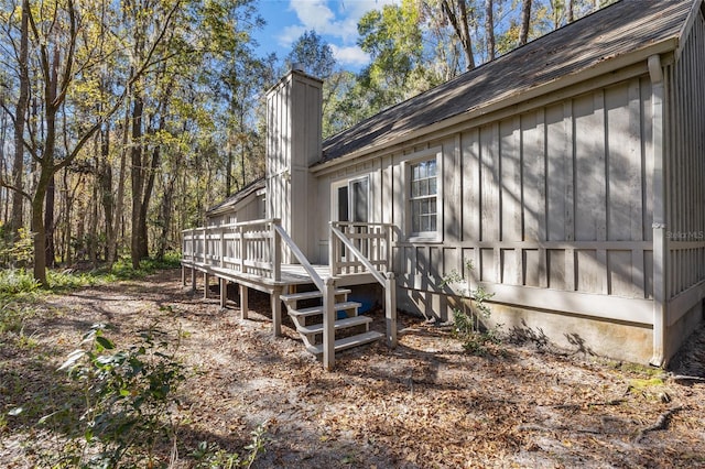 view of side of home featuring a deck, board and batten siding, and a chimney