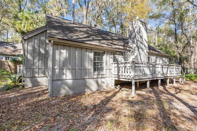 view of side of property with board and batten siding, a chimney, roof with shingles, and a deck