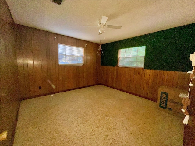 unfurnished room featuring ceiling fan, a wealth of natural light, and wood walls