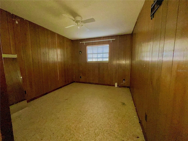 unfurnished room with ceiling fan and wood walls