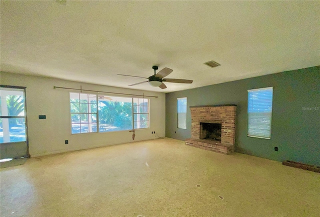 unfurnished living room featuring ceiling fan, a healthy amount of sunlight, a textured ceiling, and a brick fireplace