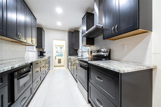 kitchen featuring light stone countertops, appliances with stainless steel finishes, tasteful backsplash, sink, and wall chimney range hood