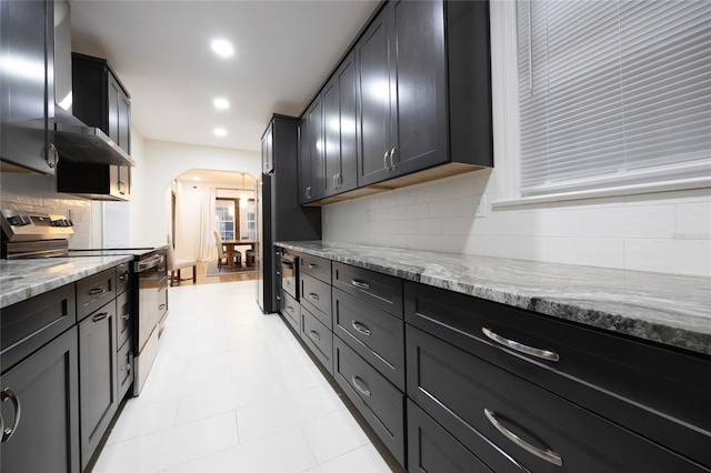 kitchen featuring backsplash, wall chimney exhaust hood, light stone countertops, and stainless steel range with electric cooktop