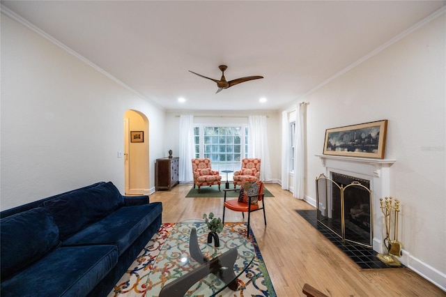 living room featuring ceiling fan, light wood-type flooring, a fireplace, and ornamental molding