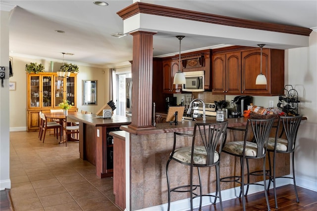 kitchen with pendant lighting, kitchen peninsula, appliances with stainless steel finishes, and decorative columns