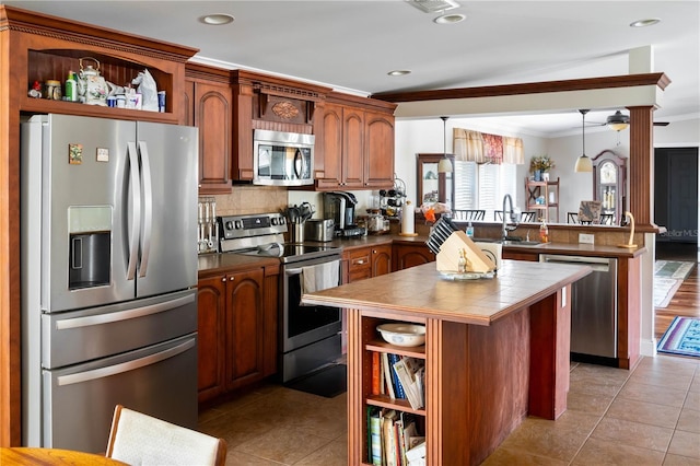 kitchen with kitchen peninsula, appliances with stainless steel finishes, crown molding, light tile patterned floors, and hanging light fixtures