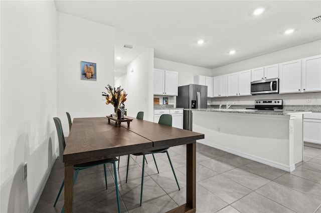 kitchen featuring a center island, white cabinets, light stone countertops, appliances with stainless steel finishes, and light tile patterned flooring