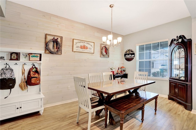 dining area featuring light wood-type flooring, a notable chandelier, and wood walls