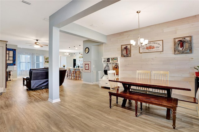 dining area with wooden walls, light hardwood / wood-style floors, and ceiling fan with notable chandelier