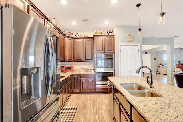 kitchen featuring sink, hanging light fixtures, stainless steel appliances, tasteful backsplash, and light stone counters