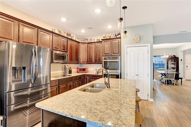 kitchen featuring a kitchen island with sink, a kitchen breakfast bar, sink, light stone countertops, and stainless steel appliances