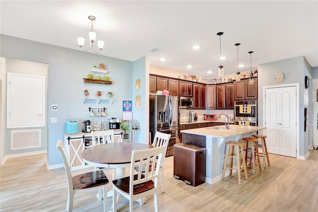 kitchen with stainless steel appliances, a kitchen island with sink, sink, decorative light fixtures, and a notable chandelier