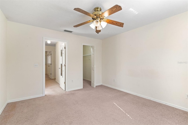 unfurnished bedroom with light carpet, a walk in closet, a closet, and ceiling fan