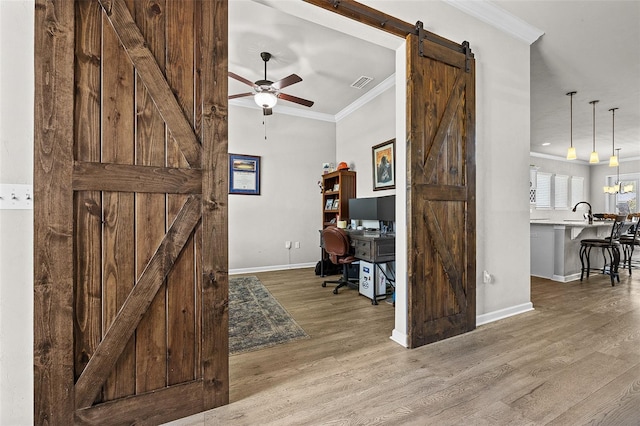 home office featuring a barn door, ceiling fan, hardwood / wood-style floors, and ornamental molding