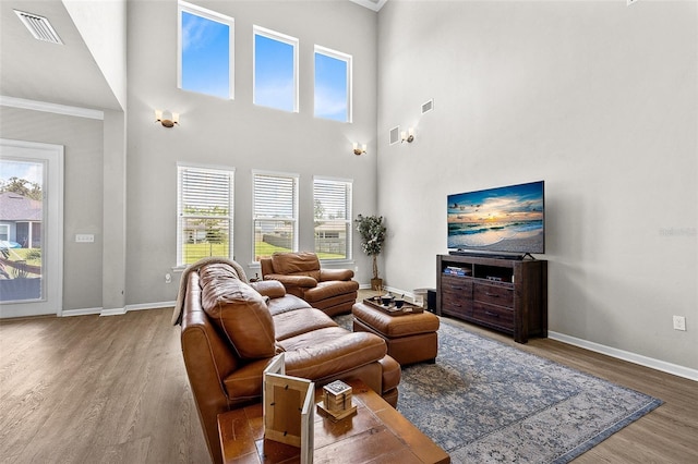 living room with hardwood / wood-style floors, a towering ceiling, and crown molding