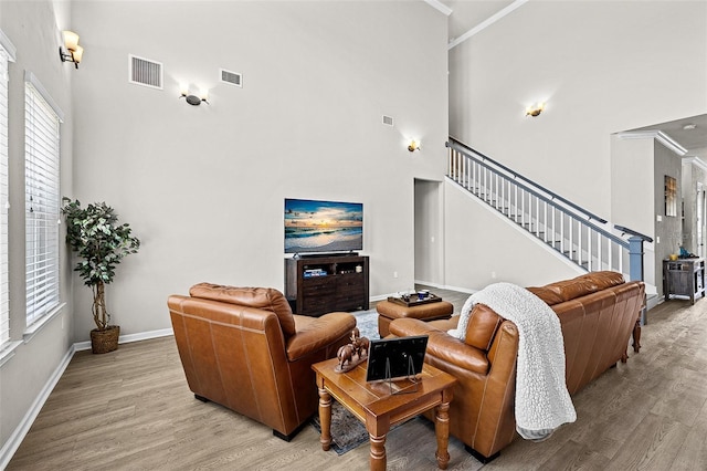 living room featuring ornamental molding, a high ceiling, and light hardwood / wood-style flooring