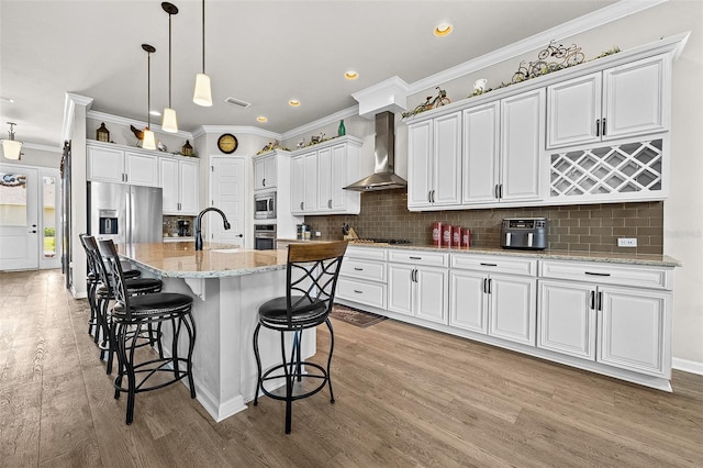 kitchen with white cabinetry, wall chimney range hood, a kitchen island with sink, and tasteful backsplash