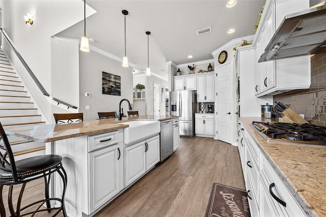 kitchen featuring white cabinetry, a kitchen island with sink, ventilation hood, decorative backsplash, and appliances with stainless steel finishes