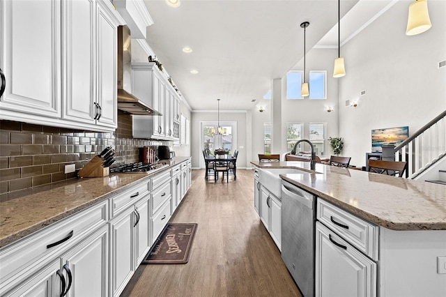 kitchen with appliances with stainless steel finishes, backsplash, wall chimney exhaust hood, a kitchen island with sink, and sink