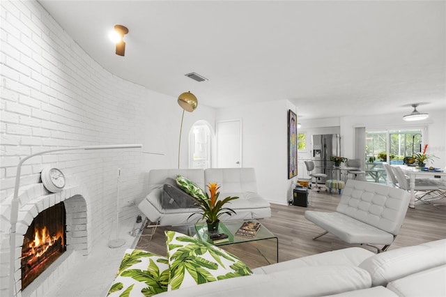 living area featuring brick wall, visible vents, a fireplace, and light wood finished floors