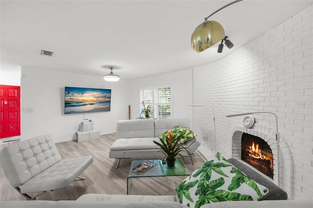 living area featuring visible vents, a brick fireplace, brick wall, light wood-type flooring, and baseboards