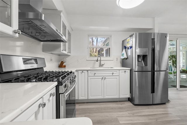 kitchen with stainless steel appliances, glass insert cabinets, white cabinetry, a sink, and wall chimney exhaust hood