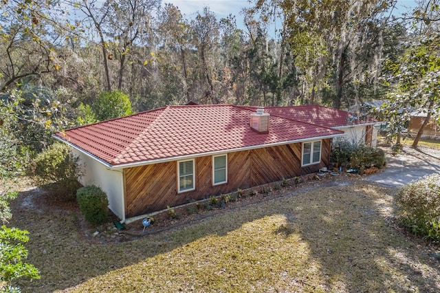 view of home's exterior with dirt driveway, a lawn, and a tiled roof