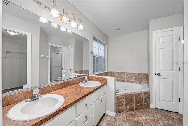 bathroom featuring toilet, vanity, a relaxing tiled tub, and tile patterned floors