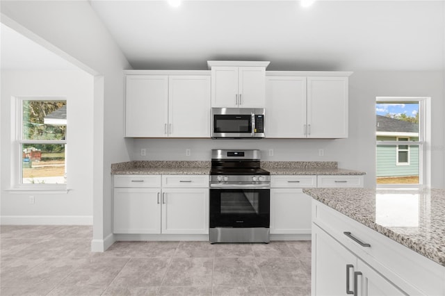 kitchen featuring white cabinets, appliances with stainless steel finishes, light stone countertops, and lofted ceiling