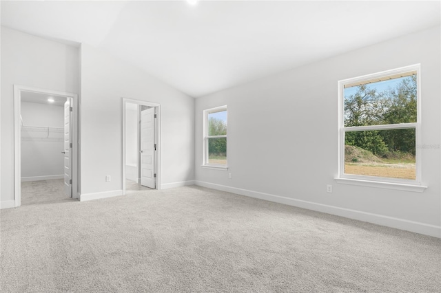 unfurnished bedroom featuring ensuite bath, lofted ceiling, a walk in closet, light carpet, and a closet