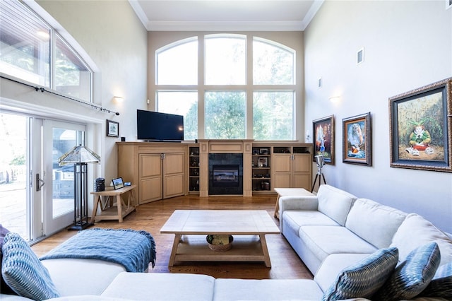 living room with a tile fireplace, crown molding, a towering ceiling, and light hardwood / wood-style floors