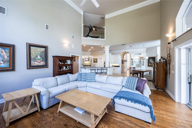 living room featuring ceiling fan, hardwood / wood-style floors, a high ceiling, and ornamental molding