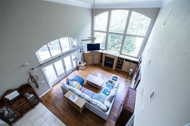 living room featuring ceiling fan, light hardwood / wood-style flooring, a high ceiling, and ornamental molding