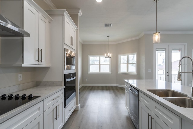 kitchen with light stone counters, wall chimney exhaust hood, stainless steel appliances, sink, and white cabinetry