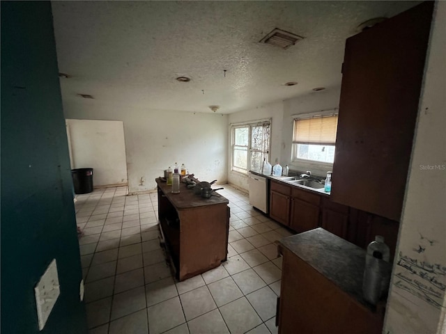 kitchen with a textured ceiling, dishwasher, a center island, sink, and light tile patterned floors