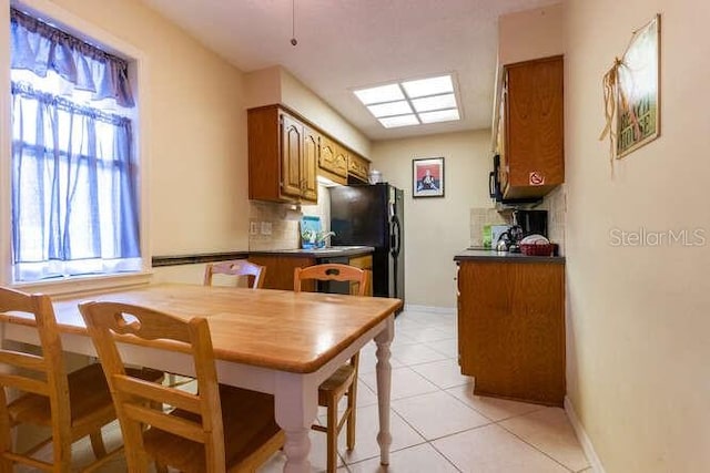 kitchen with decorative backsplash, black refrigerator, and light tile patterned floors