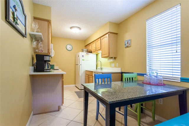 kitchen with sink, a textured ceiling, white appliances, light brown cabinetry, and light tile patterned floors