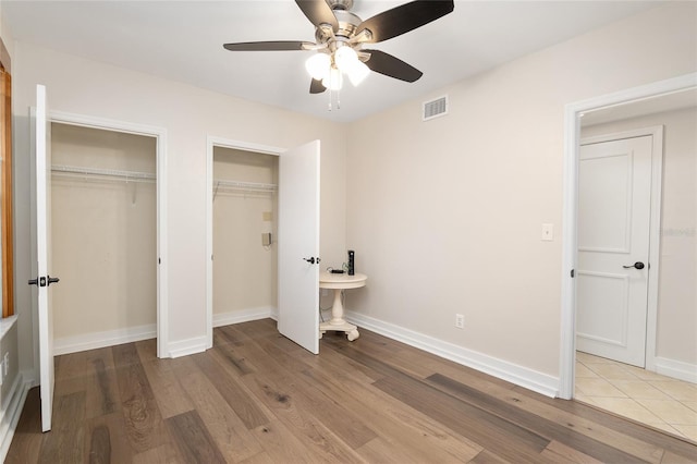 unfurnished bedroom with ceiling fan, light hardwood / wood-style floors, and multiple closets