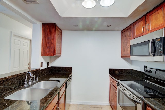 kitchen featuring light tile patterned floors, stainless steel appliances, dark stone counters, and sink