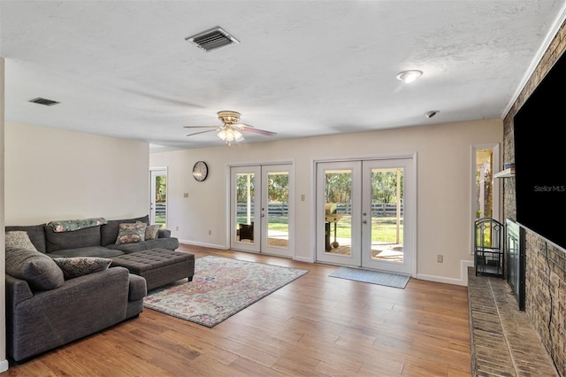 living room featuring ceiling fan, french doors, light hardwood / wood-style floors, and a textured ceiling